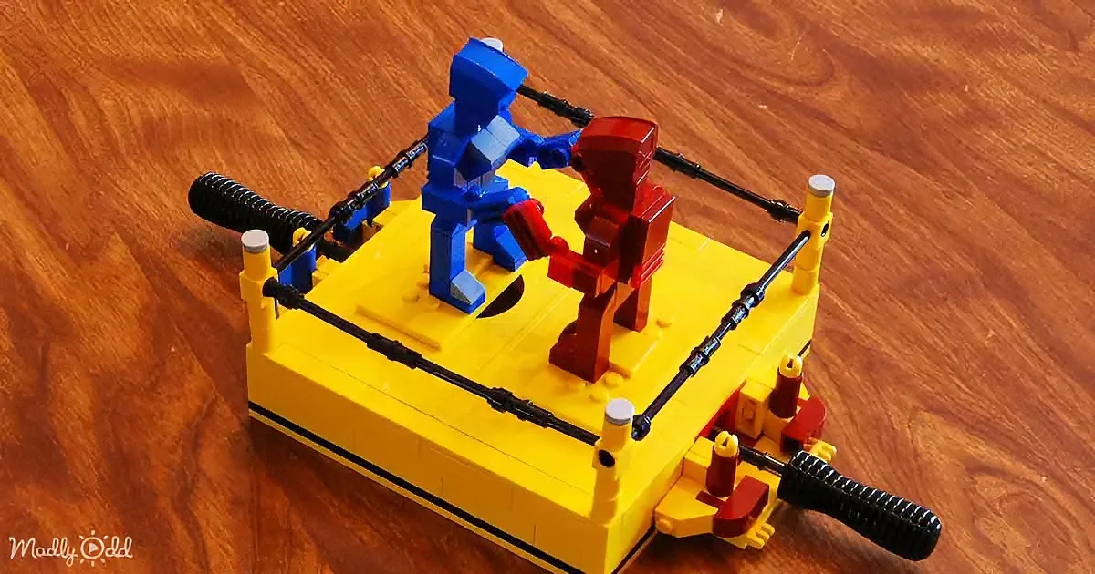 A LEGO boxing ring with two LEGO figures in a boxing stance, one blue and one red, on a wooden surface.
