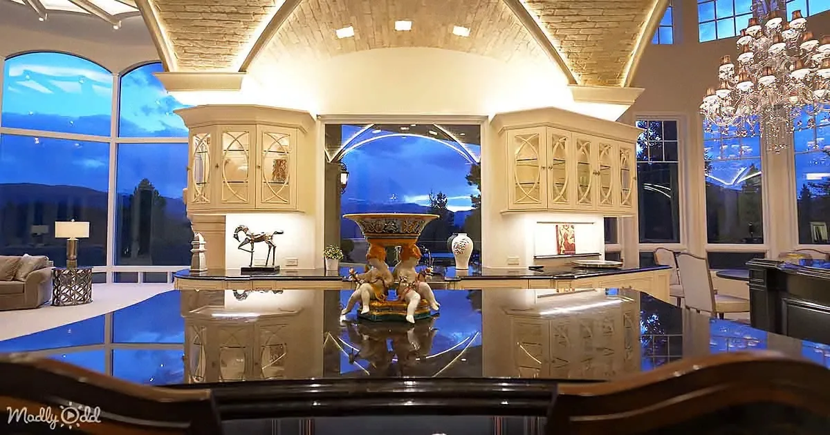 A luxurious kitchen with a central fountain, ornate cabinets, and large windows showcasing a scenic view.