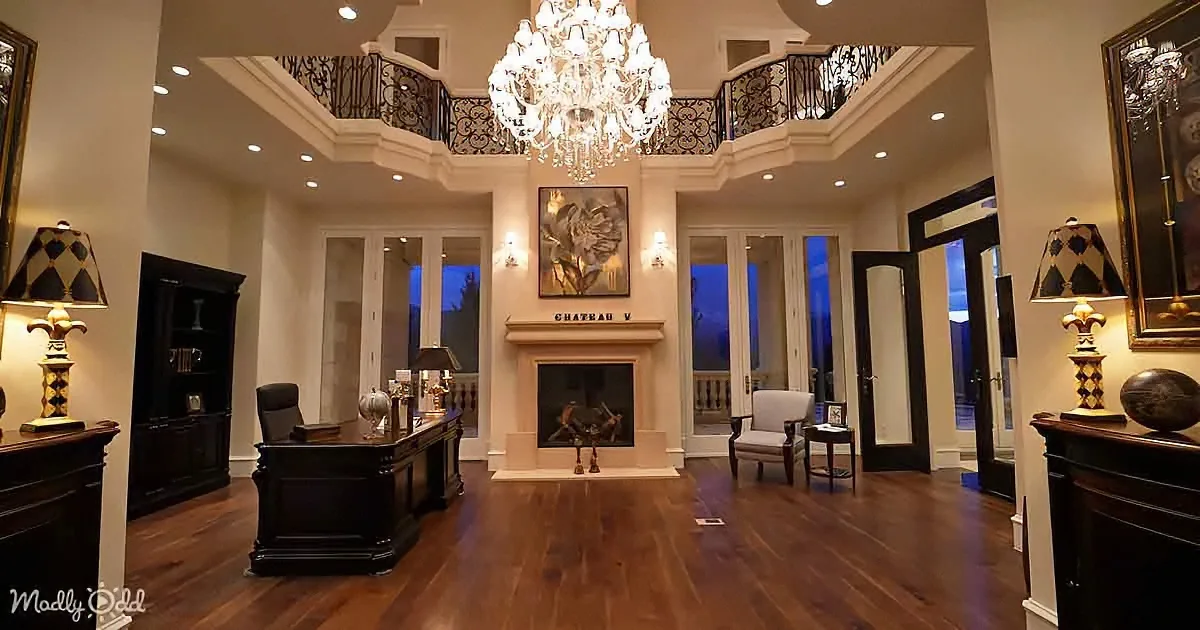 A luxurious room with a chandelier, fireplace, and elegant furniture, featuring a balcony and large windows.
