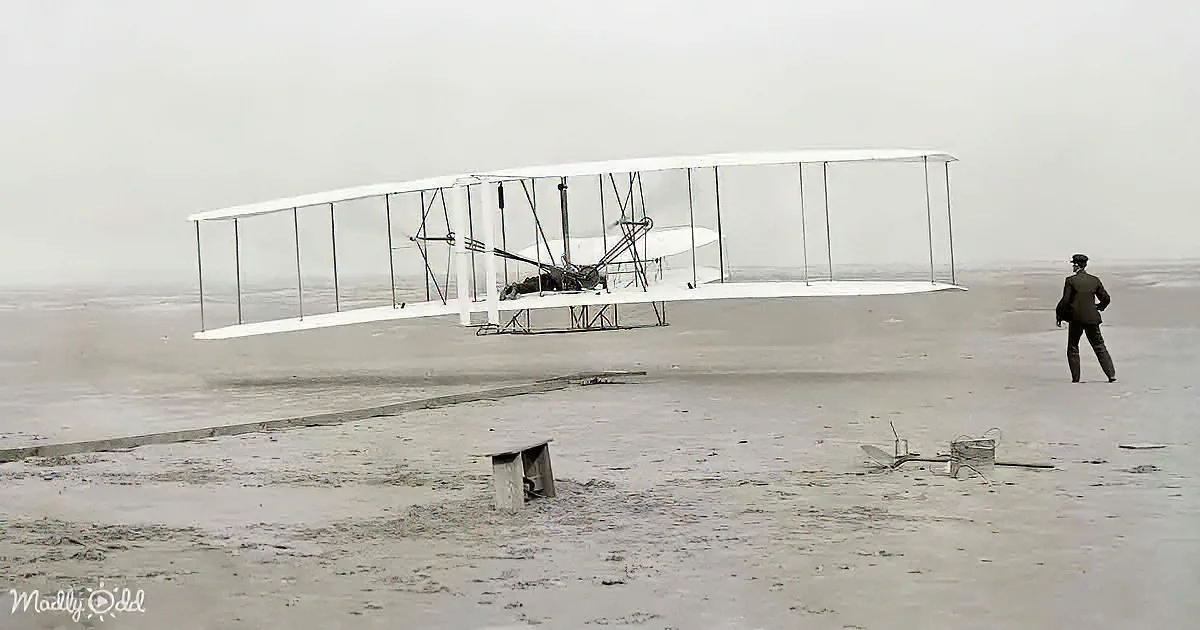 A vintage biplane with a man in a suit observing it on a sandy beach.