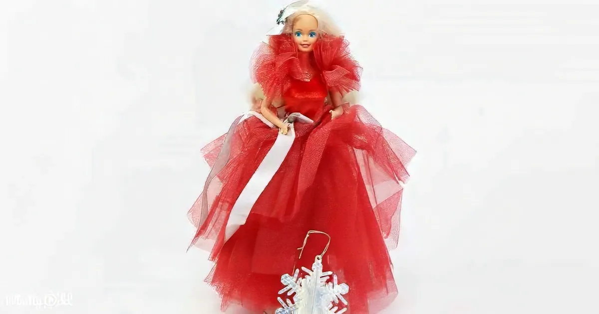 A doll in a red, sparkly dress with a white sash and a white hat with a red bow.