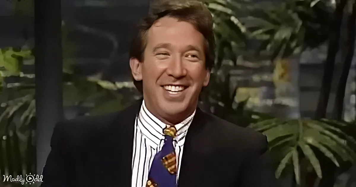 A man in a suit and striped shirt smiles brightly, with tropical plants in the background.