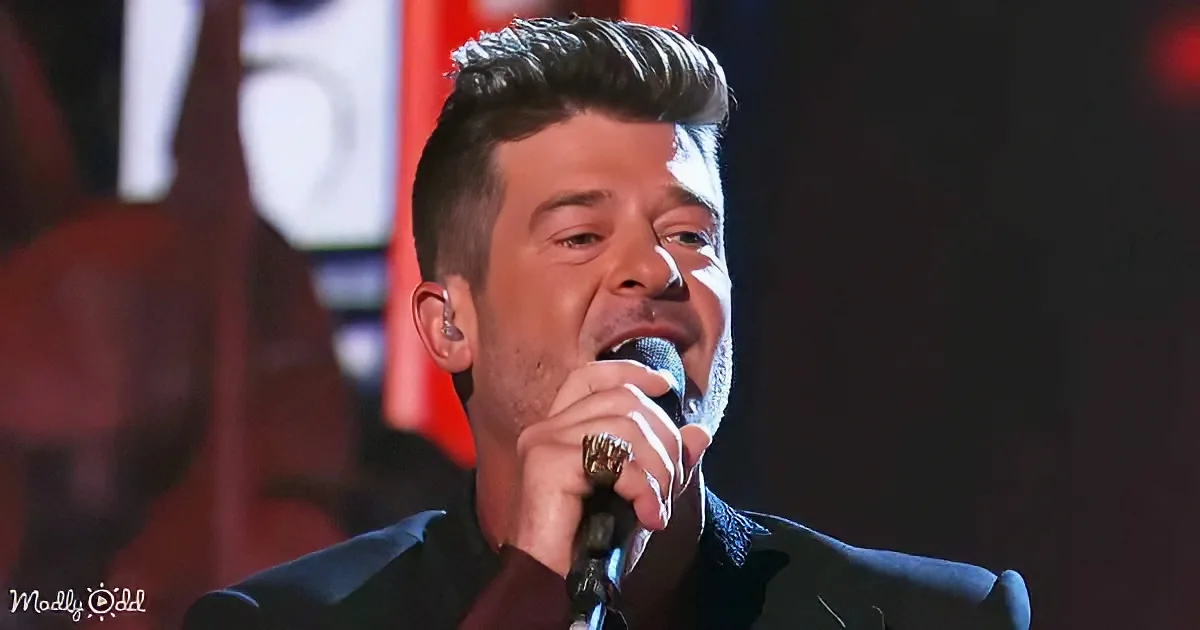 A man with short hair, wearing a suit, sings into a microphone on stage.