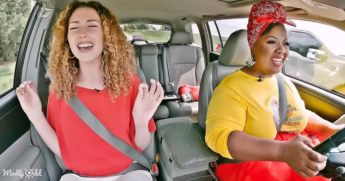 Two women are laughing in a car, one in a red shirt and the other in a yellow shirt with a bandana.