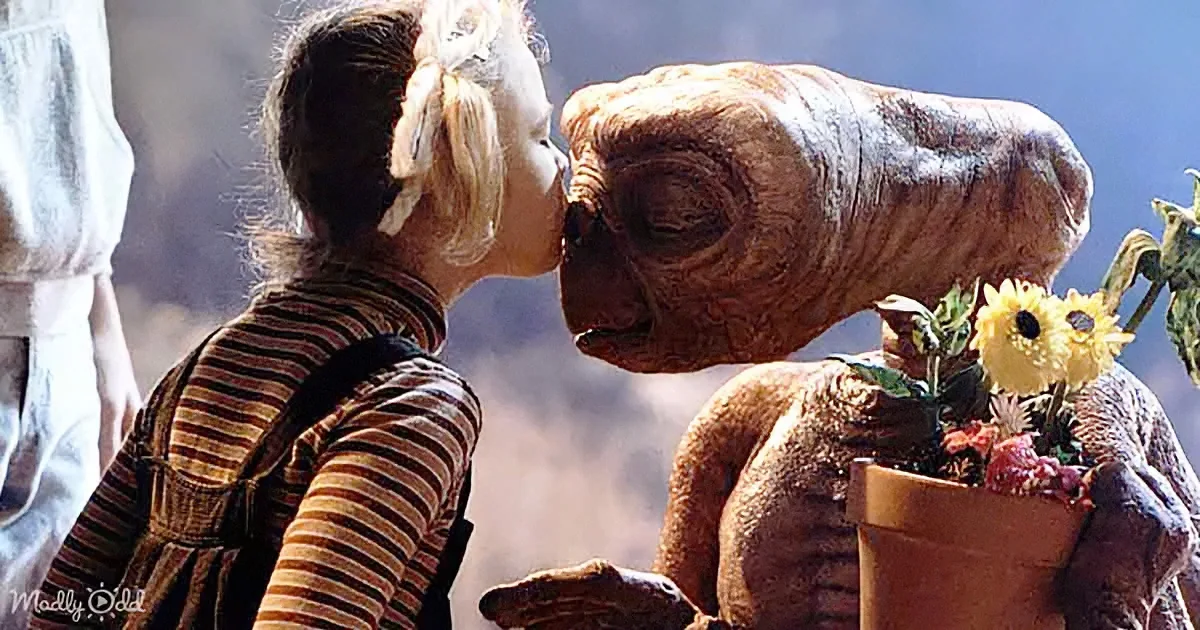 A young girl kisses E.T. on the cheek while holding a basket of flowers.