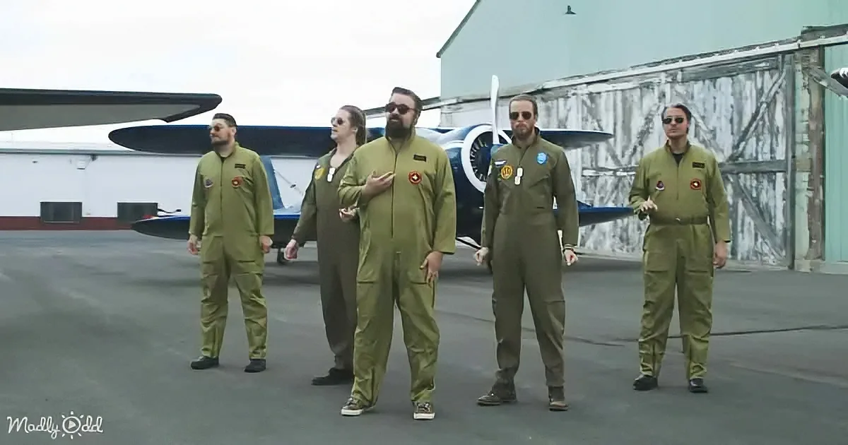 Five individuals in flight suits stand in front of a small airplane on a tarmac.