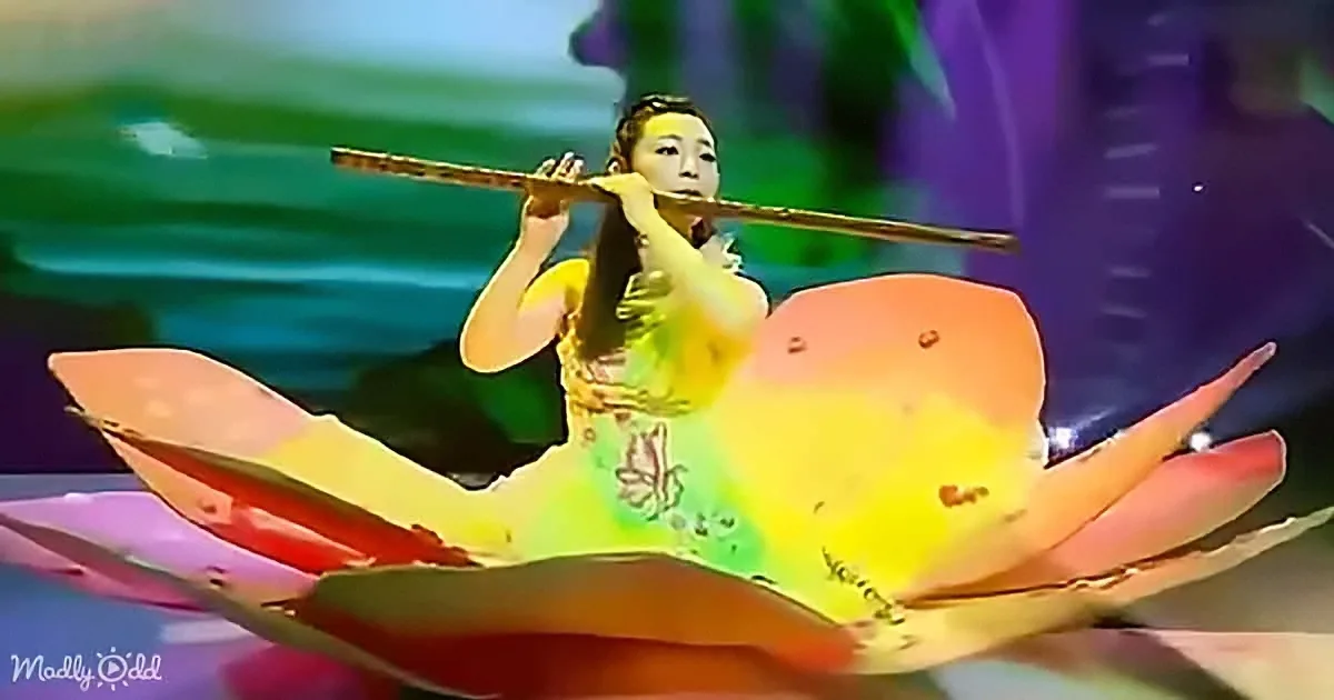 A woman plays a flute, surrounded by vibrant, abstract flower petals in a colorful, surreal setting.