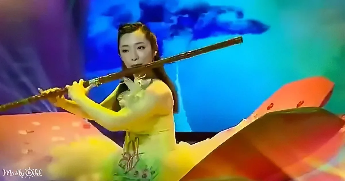 A woman in a yellow dress plays a flute against a vibrant, colorful background with abstract shapes.