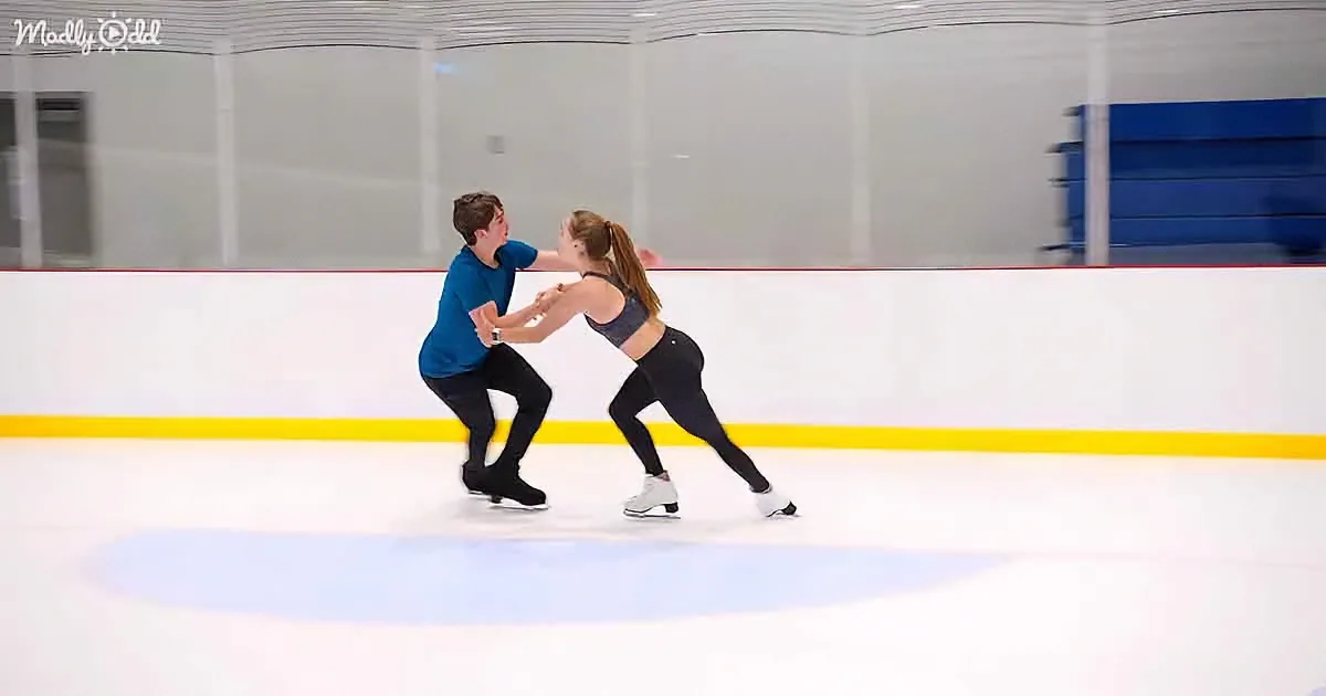 A man and woman skate in sync on an ice rink, holding hands and performing a coordinated move.