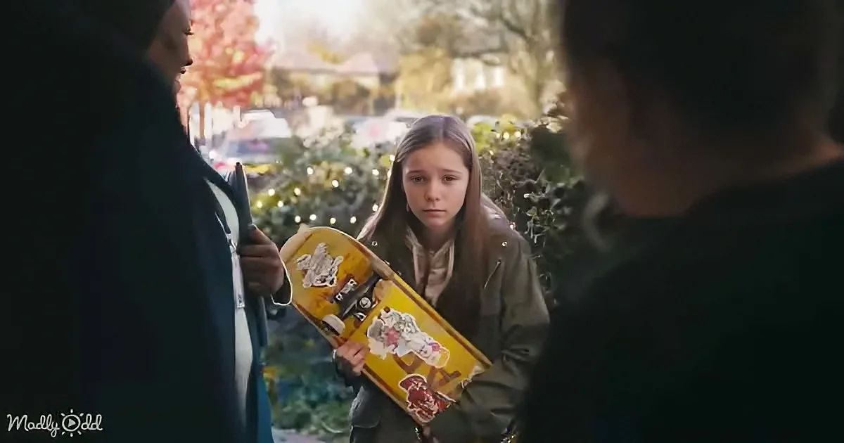 A girl with a skateboard stands between two people, looking concerned, in a park setting.