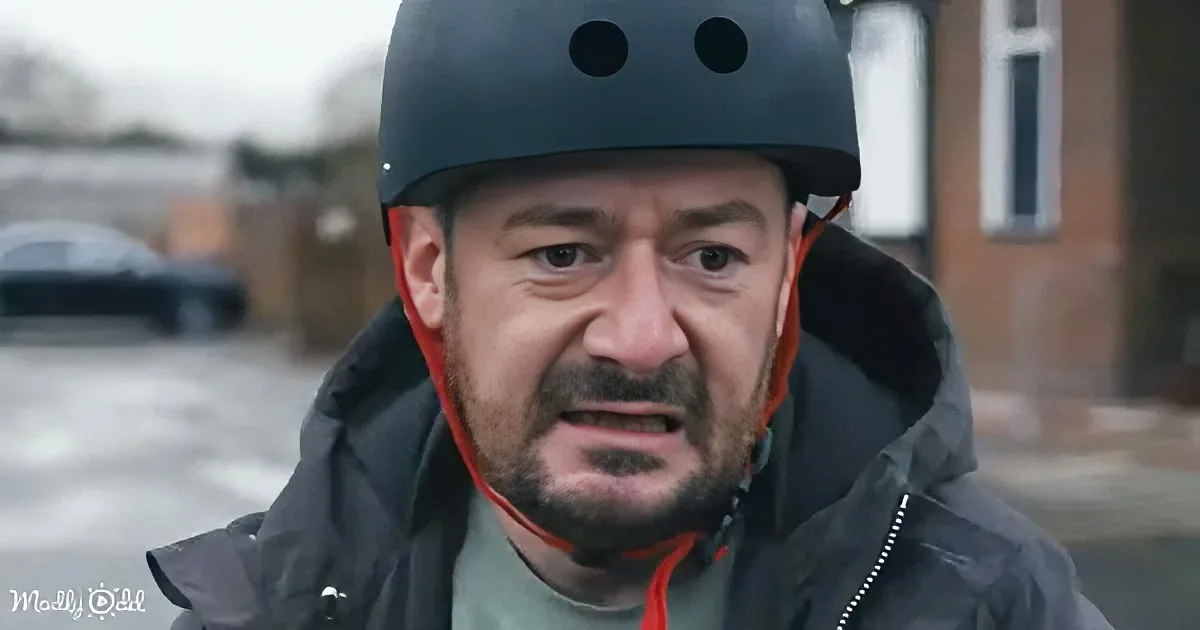 A man wearing a black helmet and dark jacket stands outdoors, looking slightly to the side.