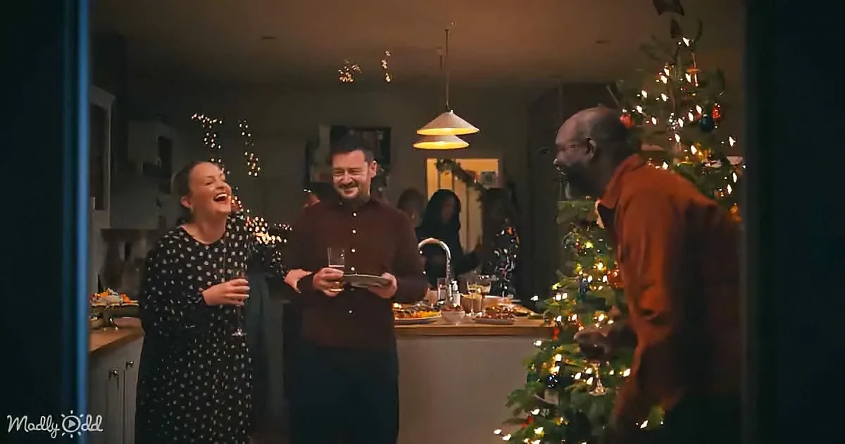 A woman in a polka-dot dress laughs while holding a glass, with a man in a brown shirt holding a plate, and another man...