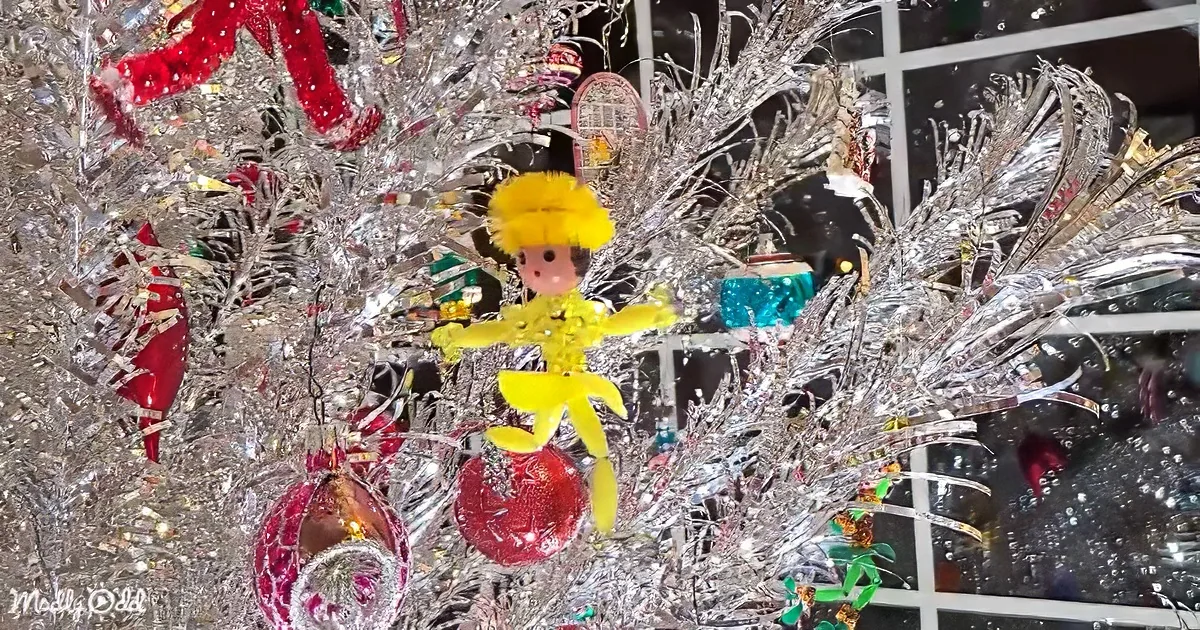 A festive Christmas tree adorned with shiny ornaments, including a yellow angel and red baubles, sparkles brightly.