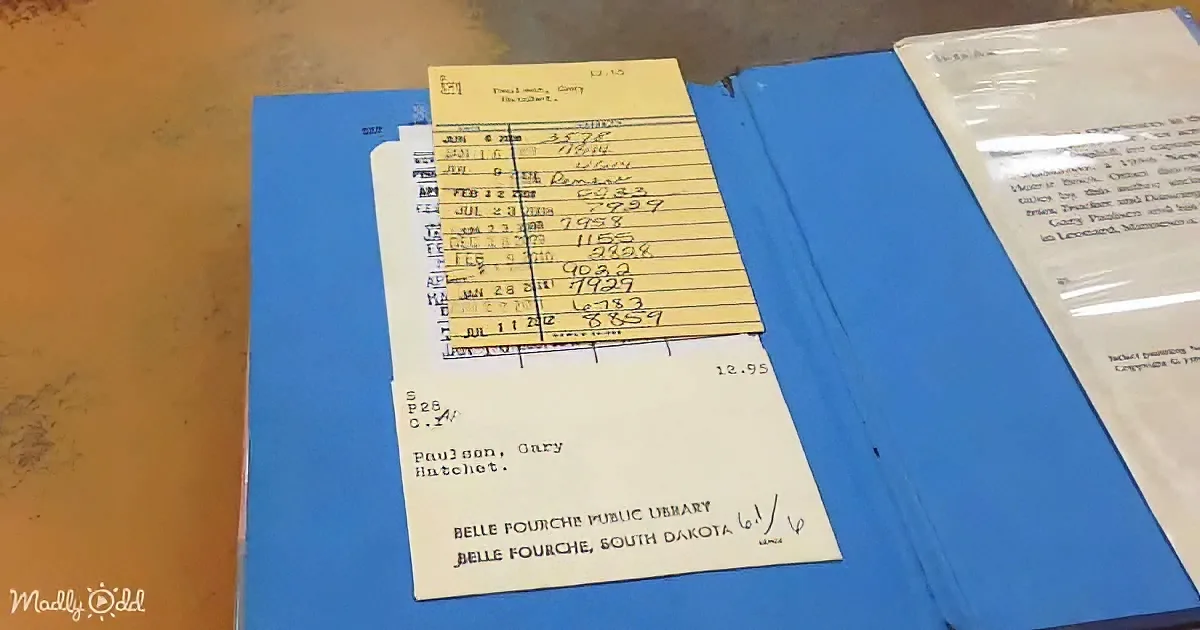 A library card and receipt for "Hatchet" by Gary Paulsen are placed on a blue folder.