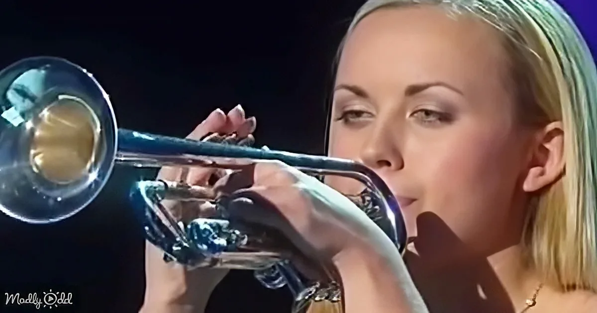 A person with blonde hair is playing a trumpet, focusing intently on the instrument.