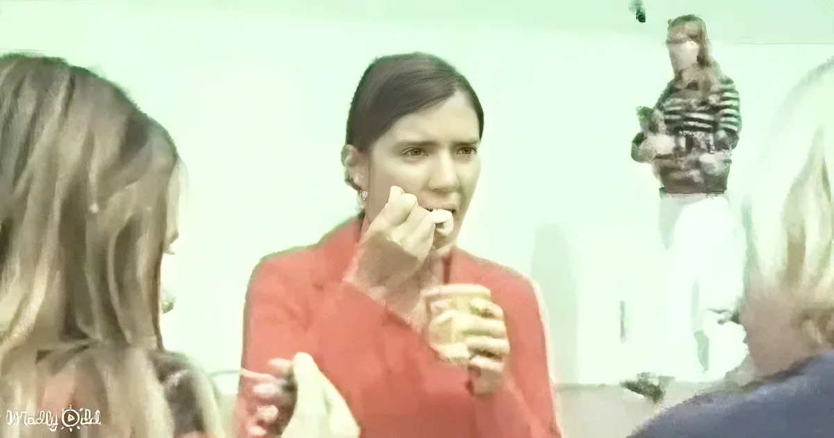 A person in a red shirt is eating while holding a drink, with others in the background.