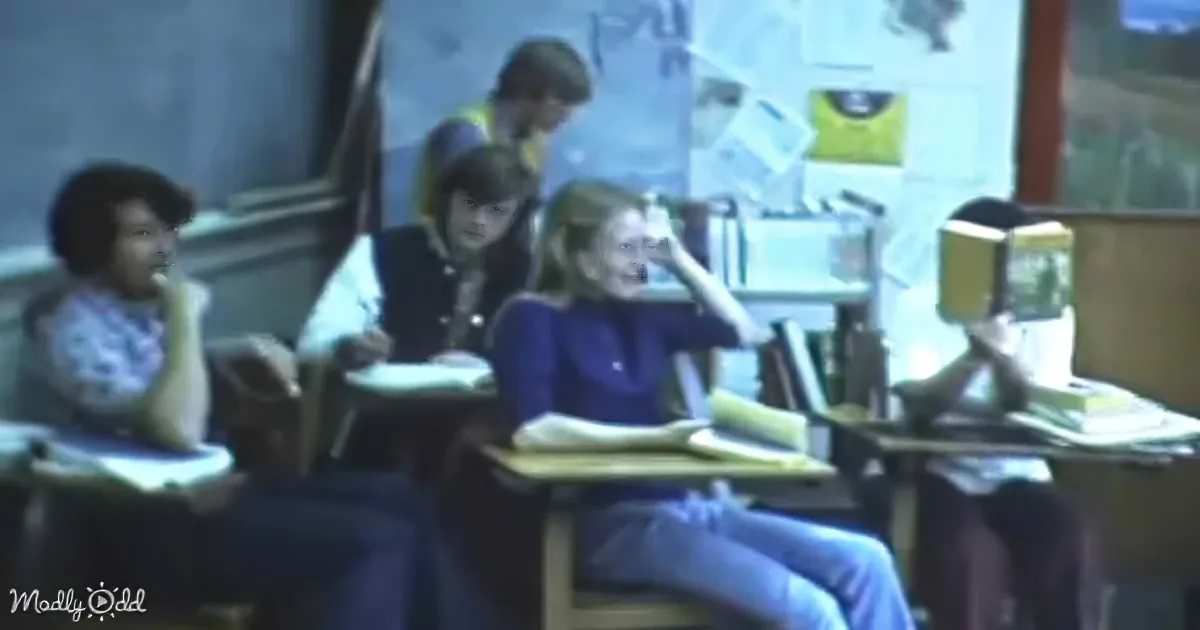 A student in a classroom is laughing while others sit at desks, one appearing to be asleep.