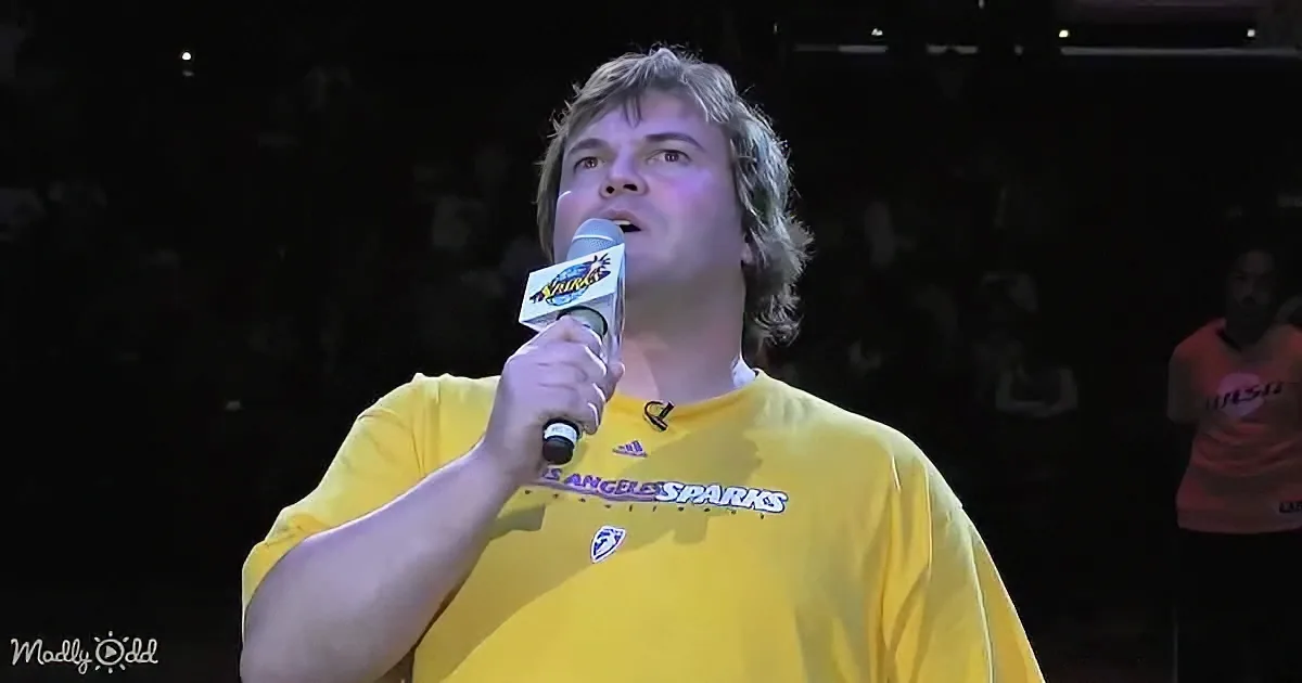 A man in a yellow "Los Angeles Sparks" shirt speaks into a microphone on stage.