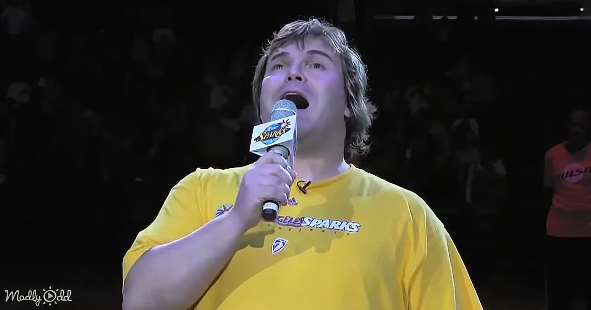 A person in a yellow "Los Angeles Sparks" shirt holds a microphone, singing or speaking on stage.