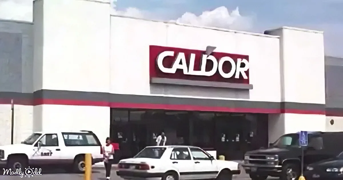 A Caldor store with a red and white sign, white building, and parked cars in front.