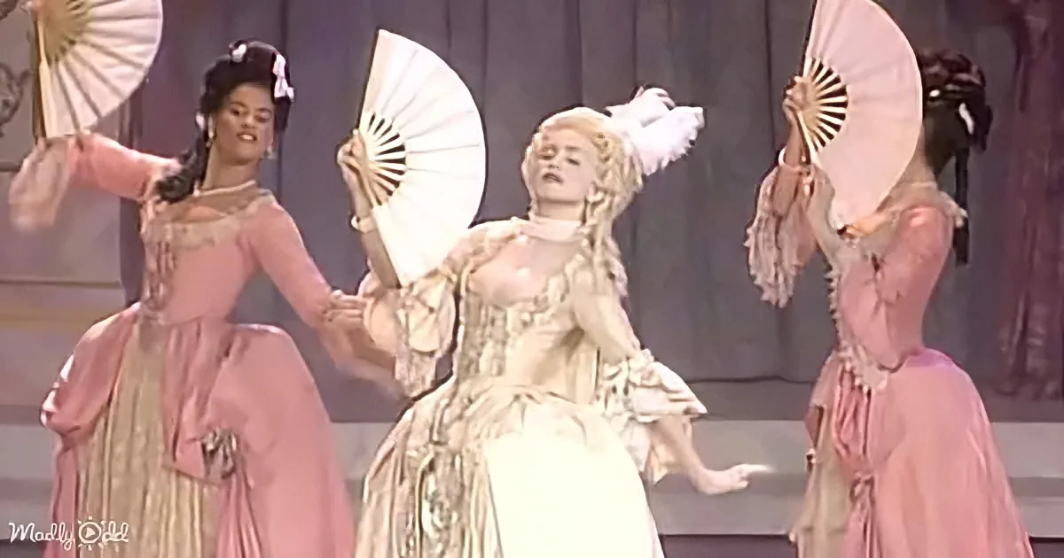 Madonna in elaborate costume with fans, surrounded by dancers in pink dresses.