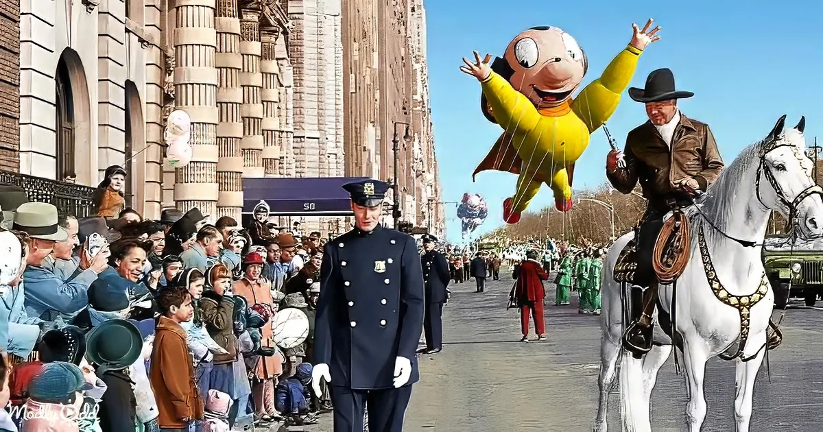 A man in a cowboy outfit rides a white horse in a parade, with a large inflatable character and a crowd of spectators.