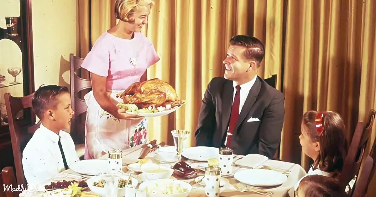 Woman in pink serves turkey to family at dining table with vintage decor.