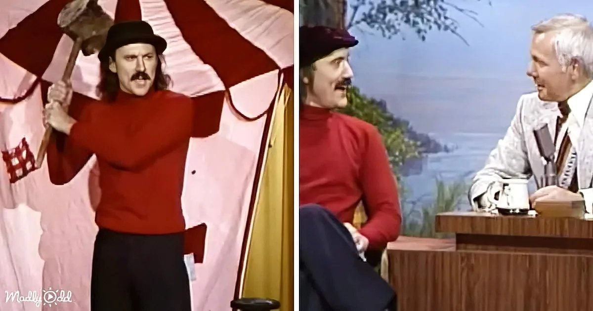 A man in a red sweater and hat holds a large hammer, standing confidently, while another man sits at a desk in a studio...