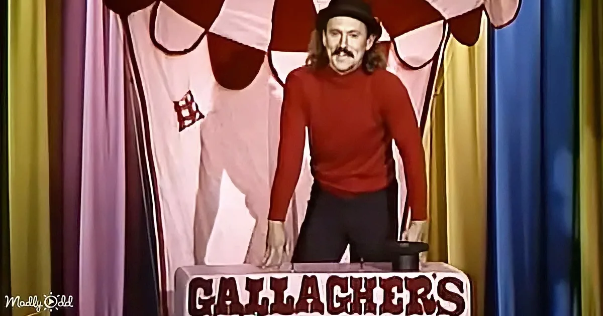 A man in a red sweater and hat stands behind a sign reading "Gallaghers" on a colorful stage backdrop.