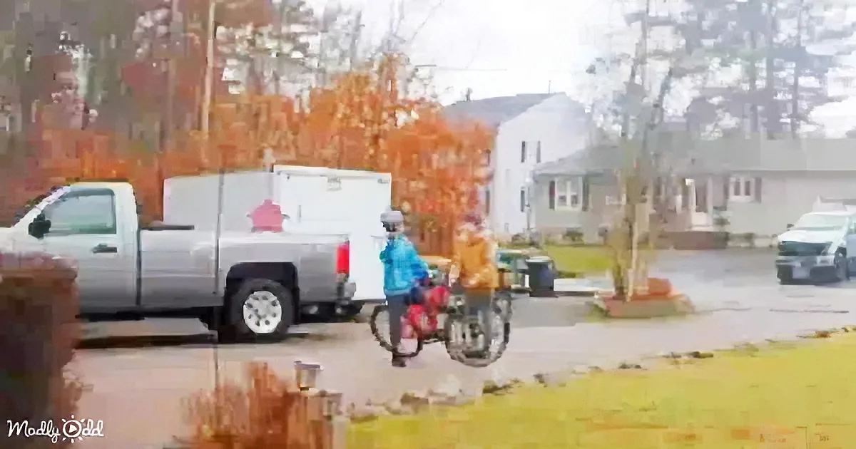 A person in a blue jacket rides a bicycle past a white truck in a residential neighborhood.