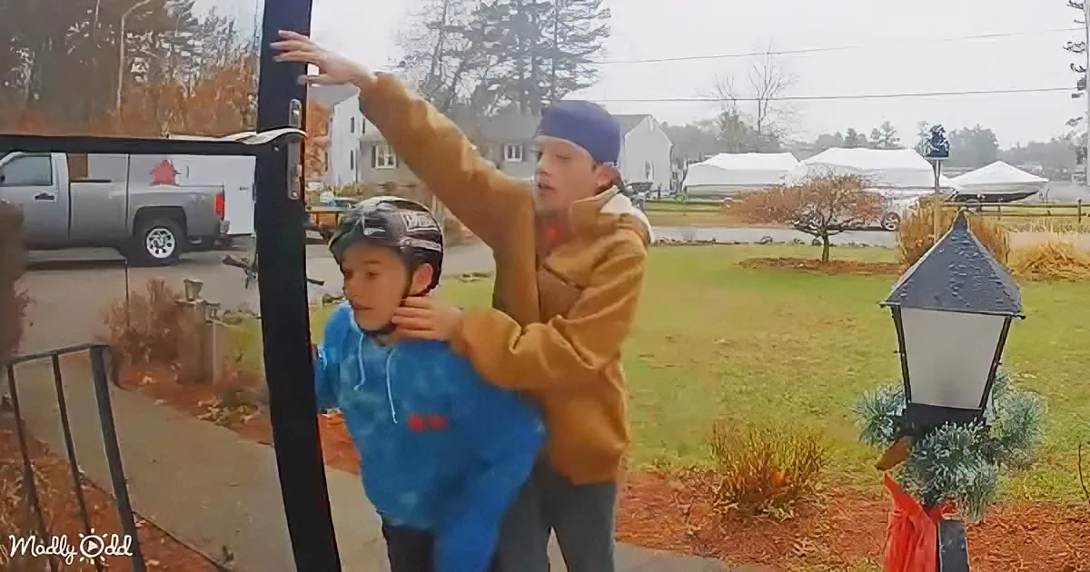 Two children, one in a blue hoodie and the other in a brown jacket, are interacting with a tall object outdoors.
