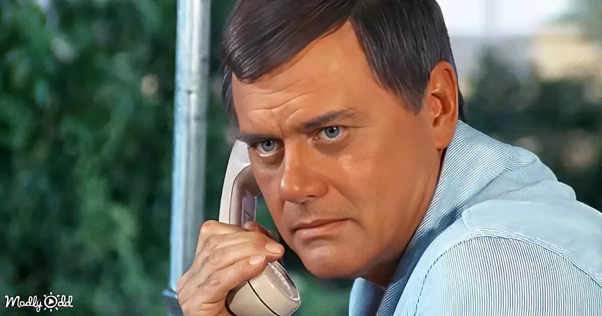 A man in a light blue shirt holds a white telephone receiver to his ear, looking concerned.