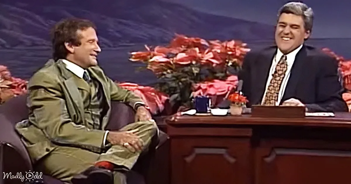Steve Carell in a green military-style jacket is seated on a couch, smiling, while Jay Leno sits at a desk, also smiling...