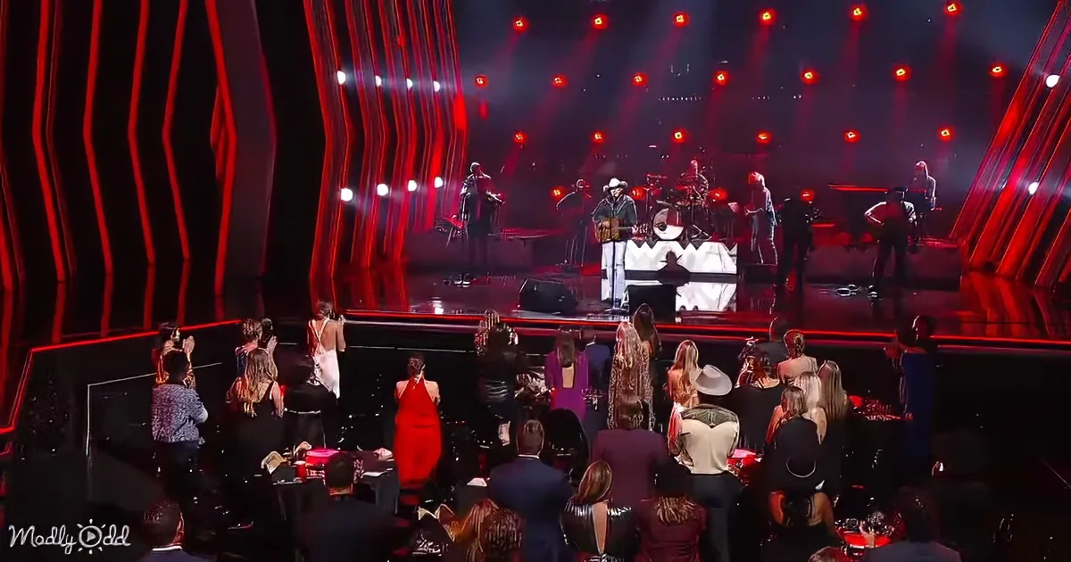 A band performs on a stage with red lighting, surrounded by an audience in formal attire.