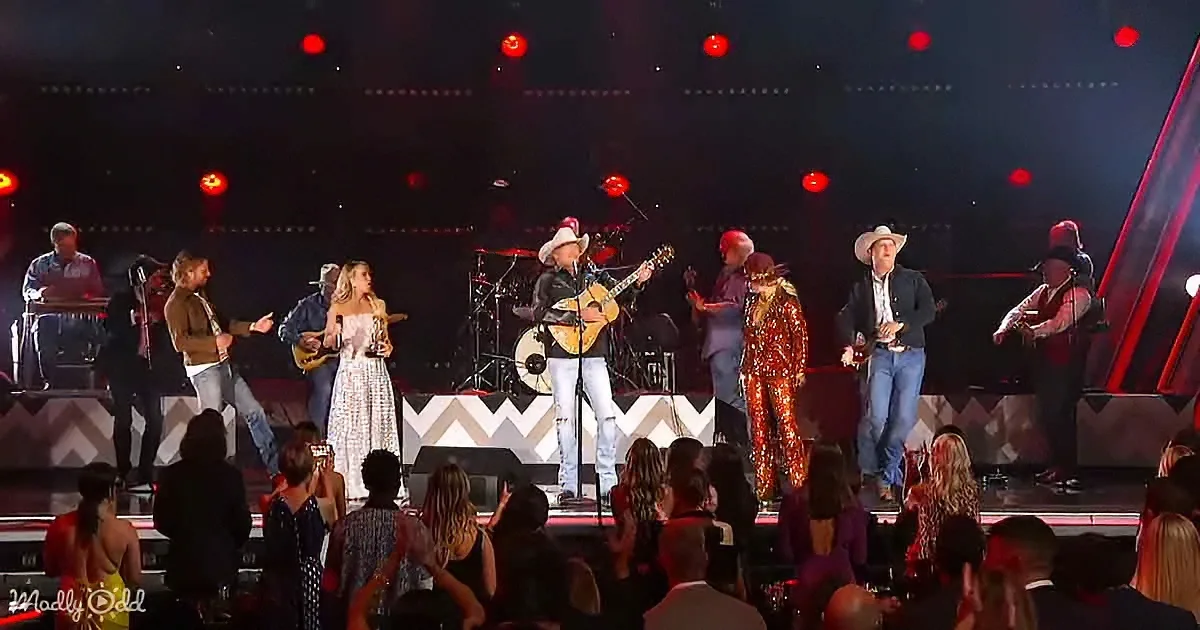 A country music band performs on stage with a female singer in a white dress, surrounded by musicians and a vibrant crowd.
