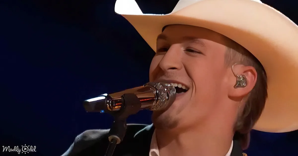 A person in a white cowboy hat sings into a microphone, smiling with eyes closed.
