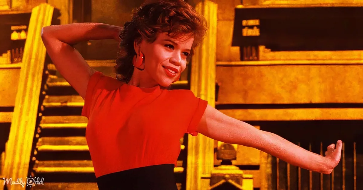A woman in a red top and black skirt smiles while striking a pose in front of a staircase.