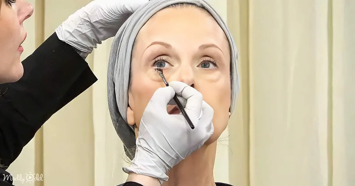 A person wearing gloves applies makeup to another person's face, focusing on the eye area.