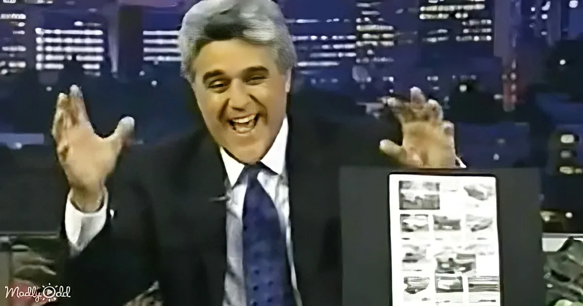 A man in a suit and tie is smiling and gesturing with his hands, with a cityscape background.