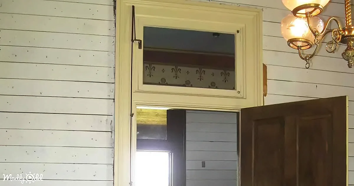 A white-framed door with a glass panel and a wooden interior door is open, revealing a light-filled room.