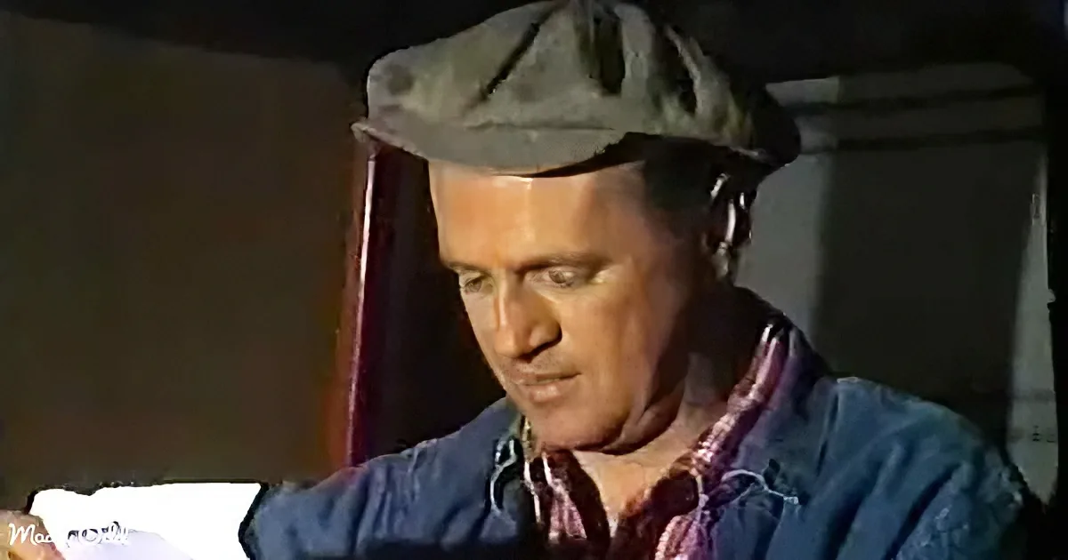 A man wearing a cap and a blue shirt is looking down, possibly reading or examining something.