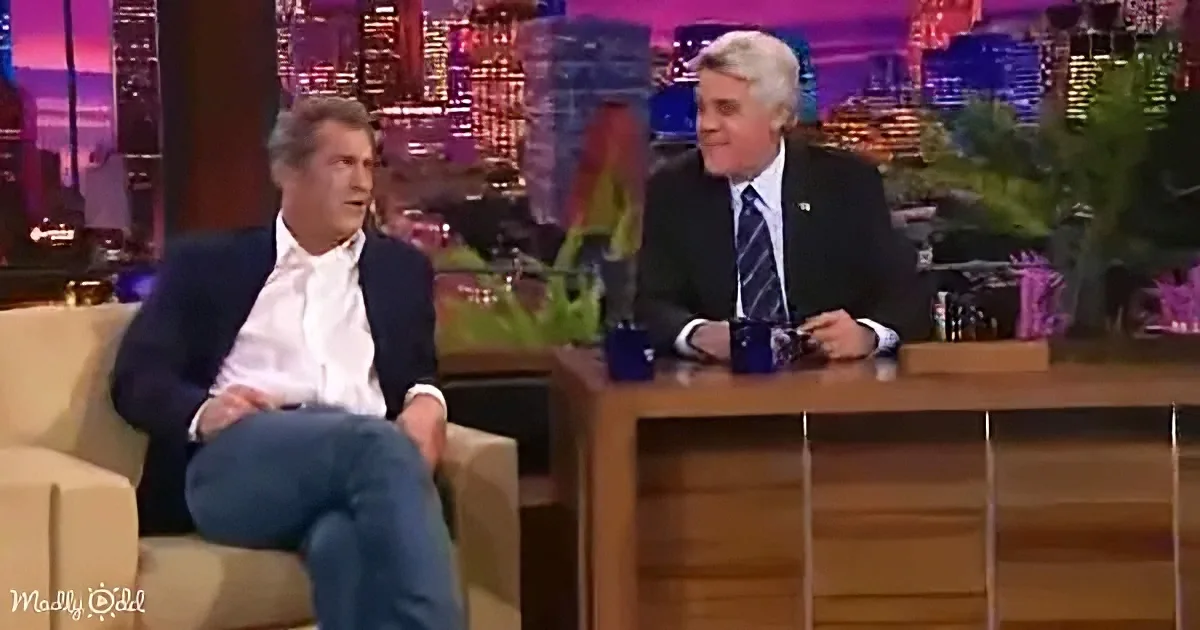 Will Ferrell sits in a chair, Jay Leno in a suit, both on a talk show set with a cityscape backdrop.