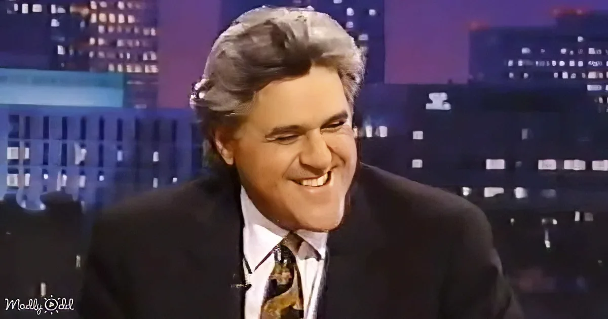 A man in a suit and tie smiles warmly, set against a cityscape backdrop.