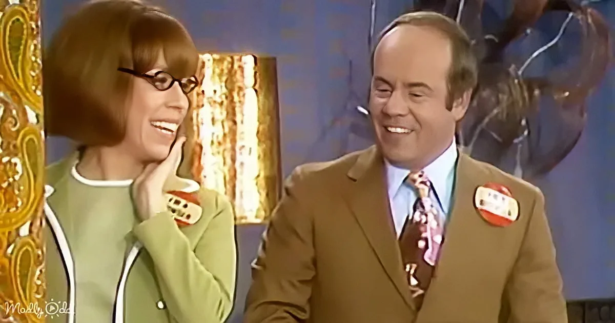 A man in a brown suit and a woman in a green jacket are smiling and laughing together.