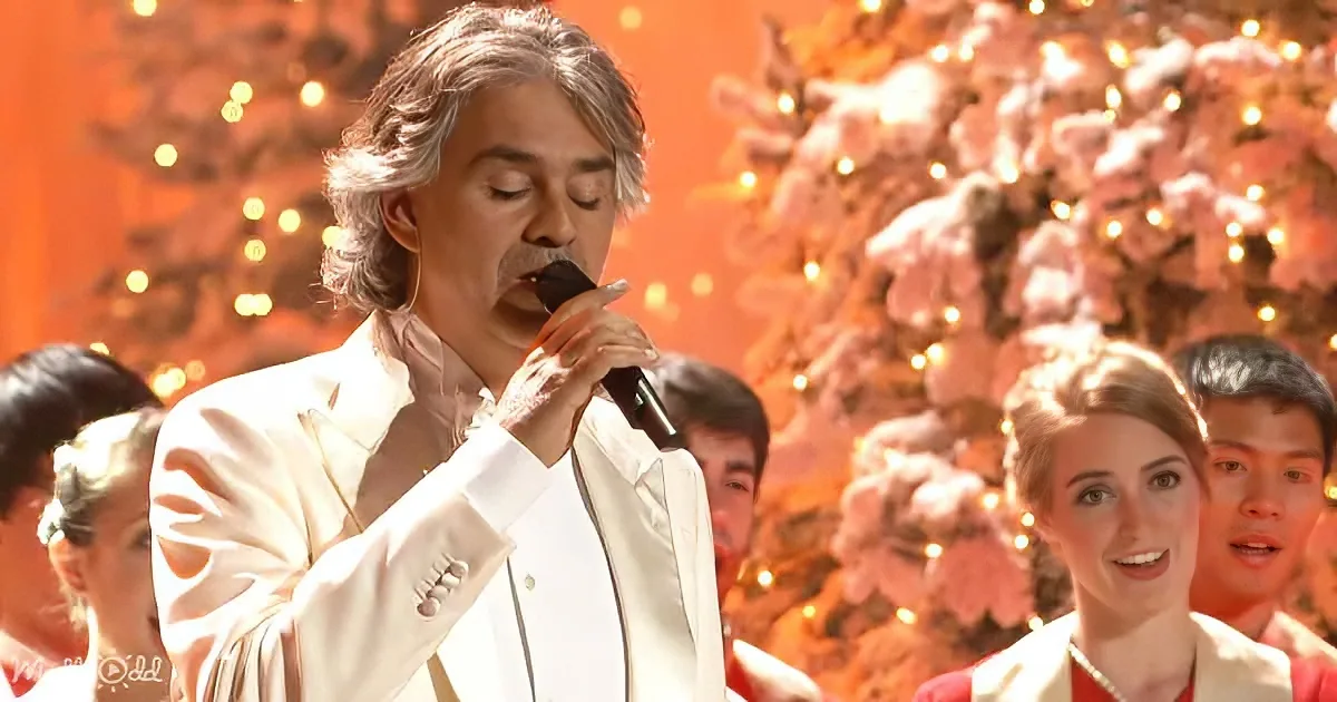 A man in a white suit sings into a microphone, surrounded by a festive Christmas setting with lights and snow.