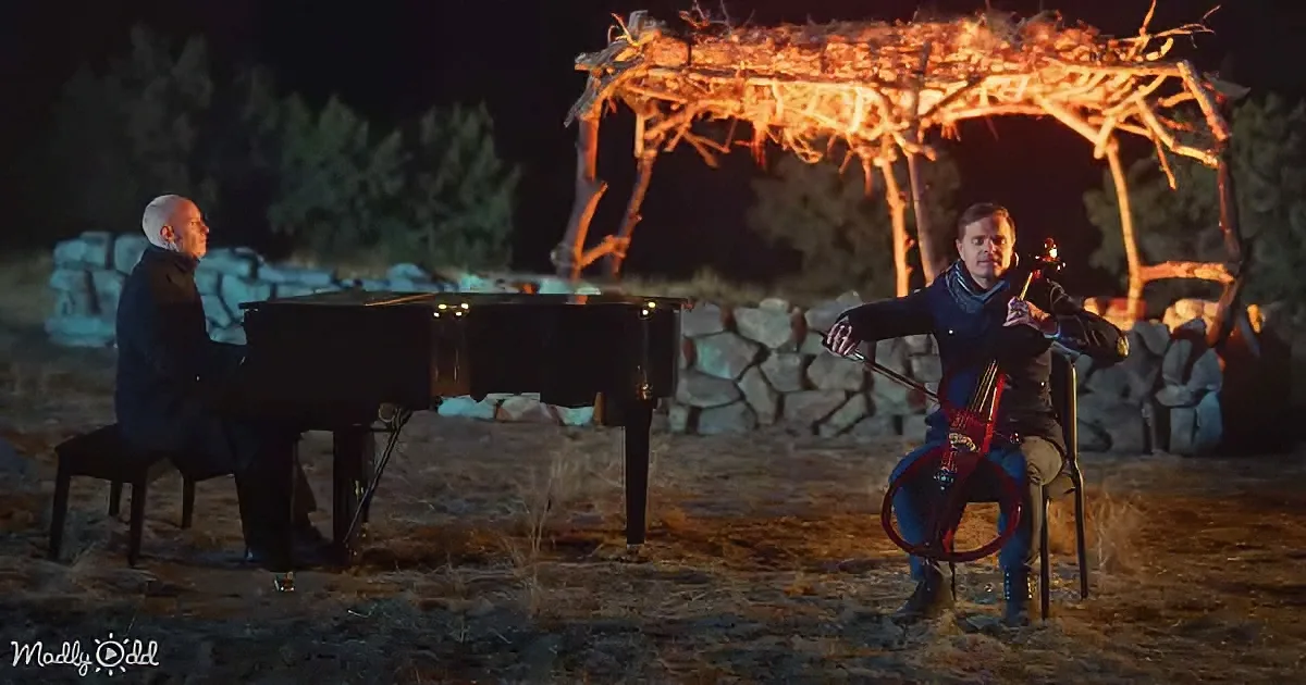 A man plays piano while another plays violin under a glowing, rustic archway at night.