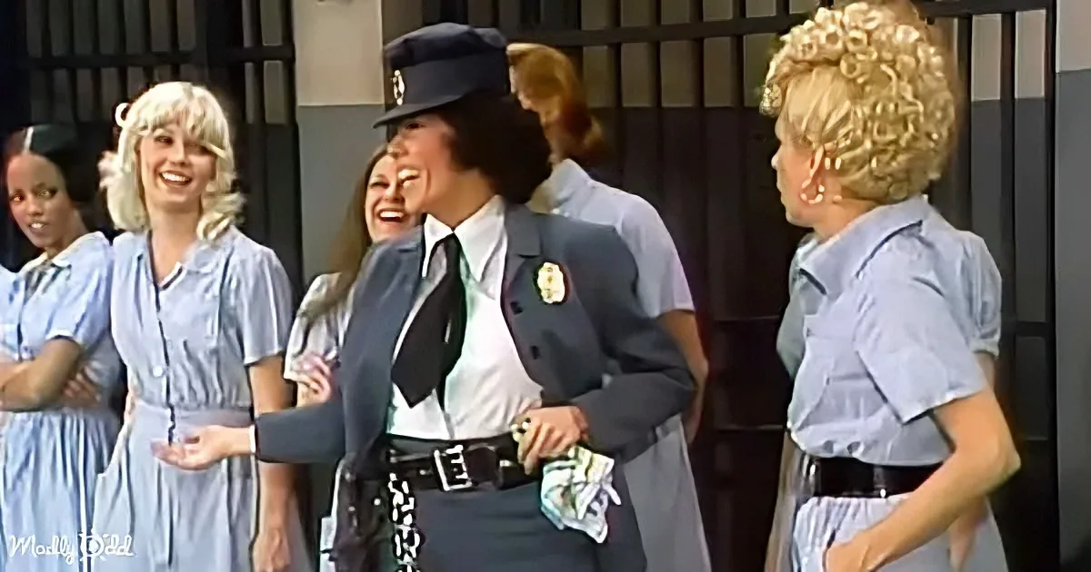 A woman in a police uniform is smiling and interacting with others in a jail setting.