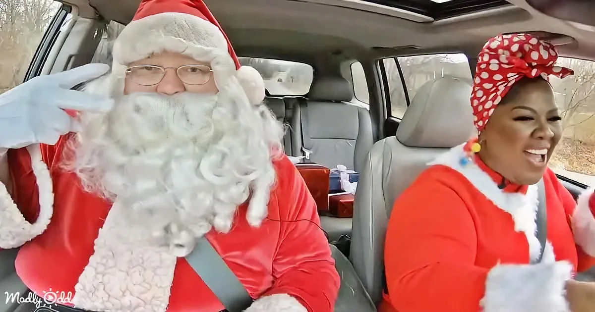 A man dressed as Santa Claus waves while sitting in a car with another person in festive attire.