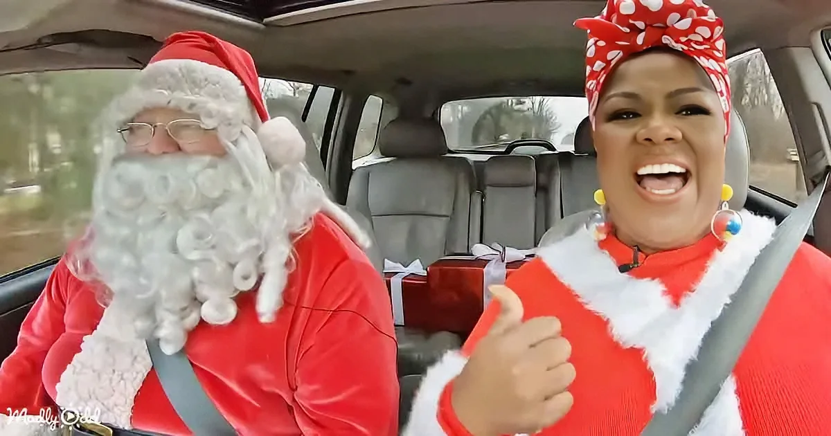 A man and woman dressed as Santa and Mrs. Claus are in a car, smiling and giving thumbs up.
