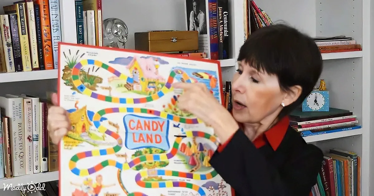 Woman holding a colorful Candy Land board game in front of a bookshelf.